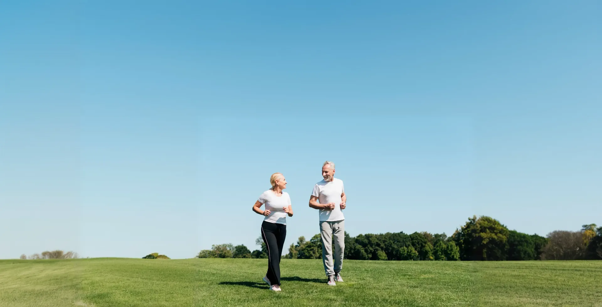 A couple walking together on grass under a clear sky